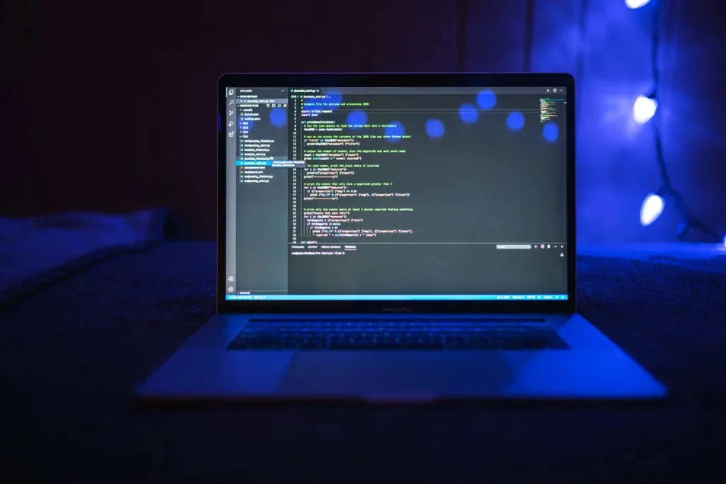 A laptop screen displaying code in an integrated development environment, set against a dark background illuminated by soft blue string lights to Write Prompts for ChatGPT